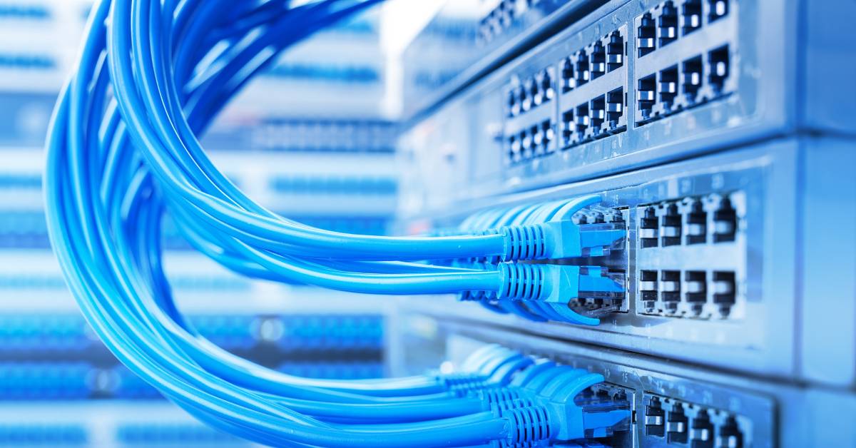 Dozens of light blue ethernet cables are plugged into stacks of network switches in a busy data center.