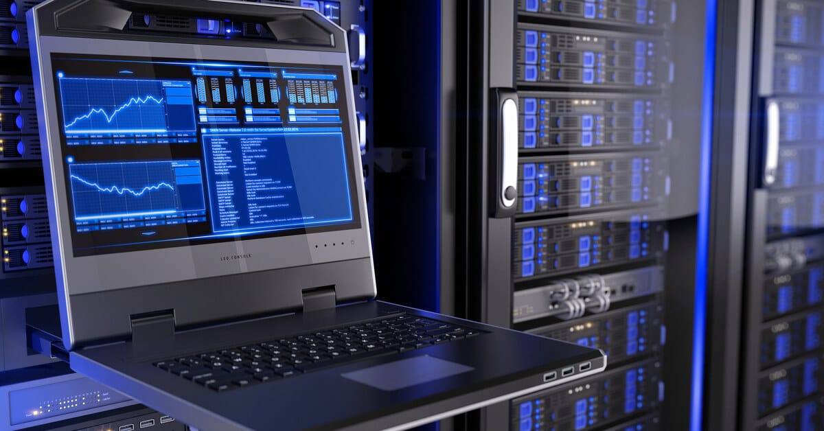 A gray laptop displaying blue charts and data. The laptop is positioned in front of black server racks with blue lights.